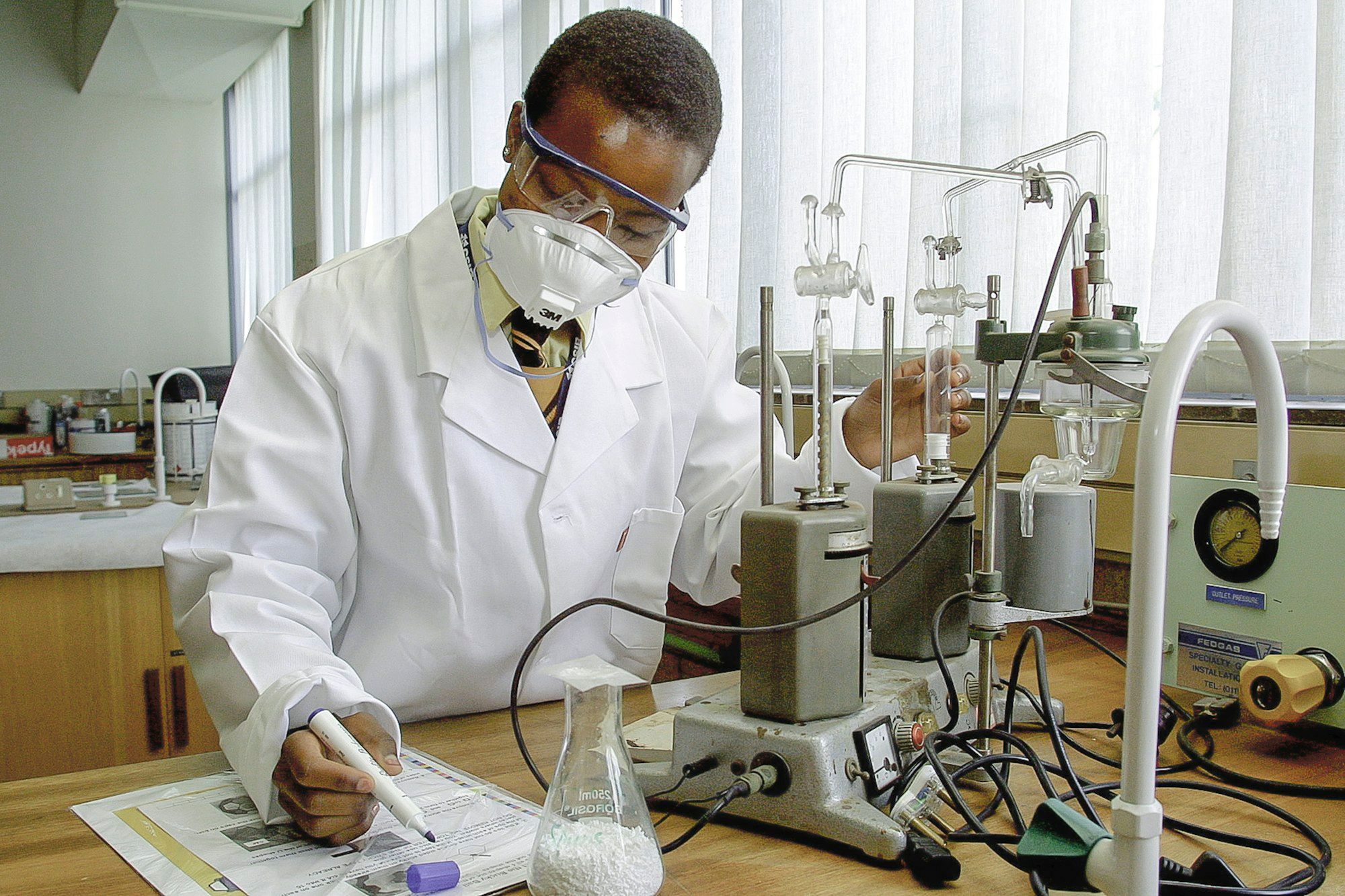 Un chercheur en blouse prend des notes à côté d’un montage d’expérience dans un laboratoire.
